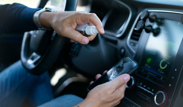 man spraying disinfectant spray on your smartphone screen inside the car