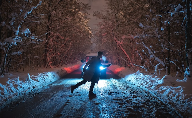 The man stand on the snowy road against the car. evening night time