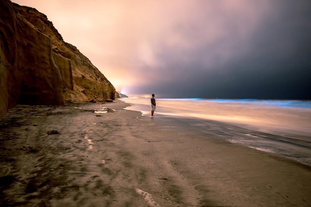 Photo man standing at beach against sky during sunset