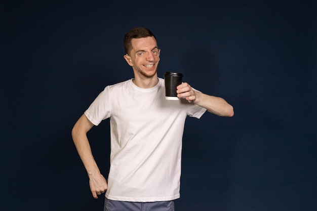 A man standing in a blue background holding a coffee in his hand