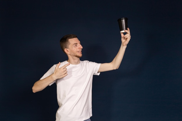 A man standing in a blue background holding a coffee in his hand