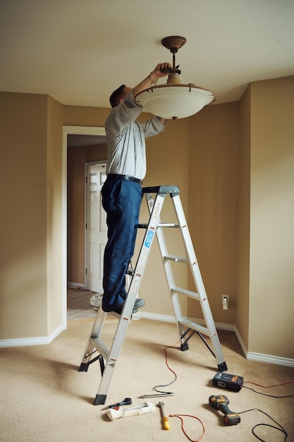 Photo man standing on a ladder to fix a ceiling fixture