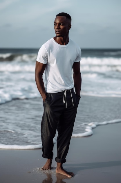 A man stands on the beach wearing a white t - shirt and black pants.