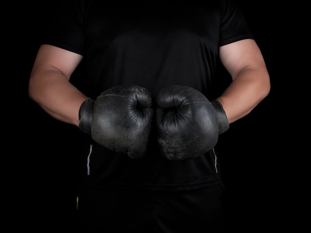 Man stands in a boxing rack, wearing very old vintage black boxing gloves