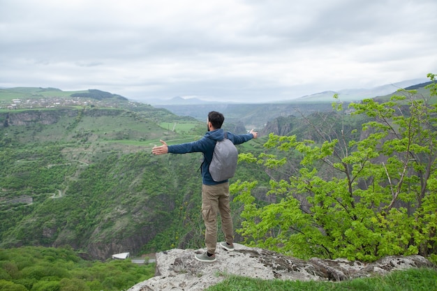 A man stands on a cliff with open hands during the day