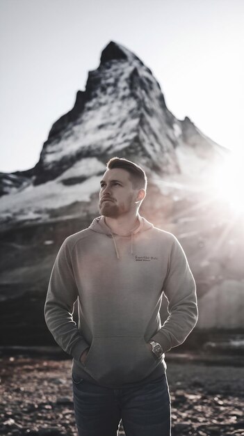 Photo a man stands in front of a mountn with the sun shining behind him