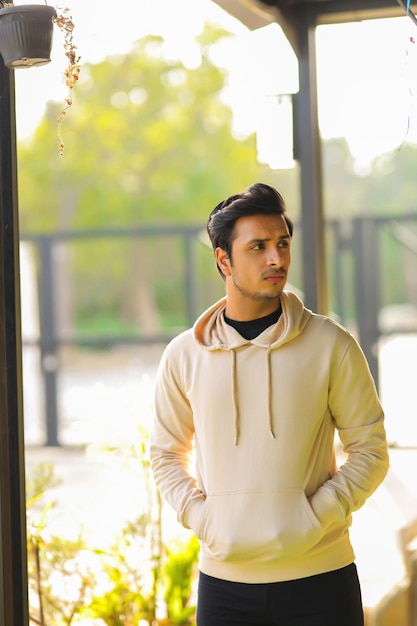 A man stands in front of a window wearing a hoodie that says'the brand is on the front. '