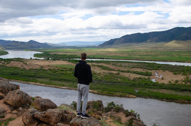 A man stands high on a hill and looks into the distance Below is the river and the mountains