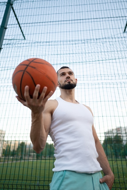 A man stands near a fence on the street, holding a basketball in his hand