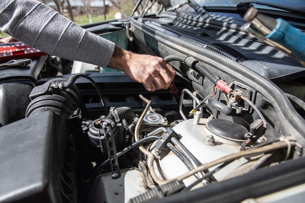 A man stands at the open hood of a car with tools