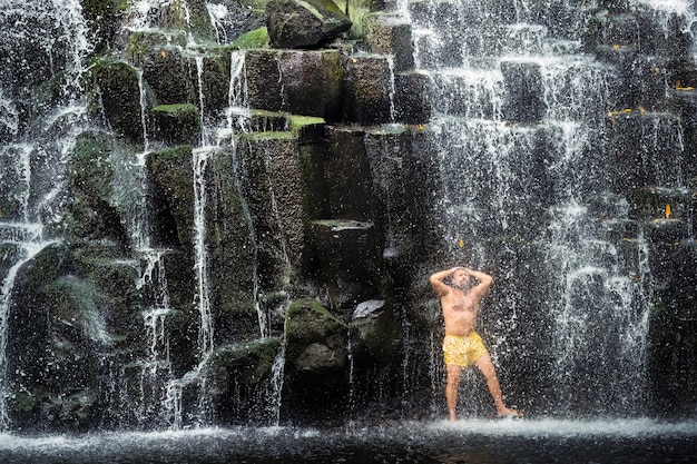 Photo a man stands under a waterfall in the jungle. a man at a cave waterfall