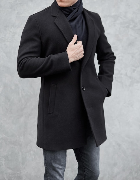 Photo man stands wearing black coat at gray background young man in classic clothes