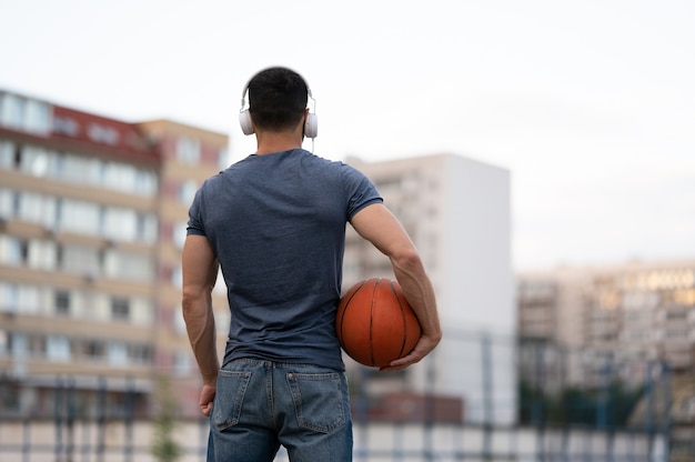 A man stands with his back of the city and holds a basketball in his hands