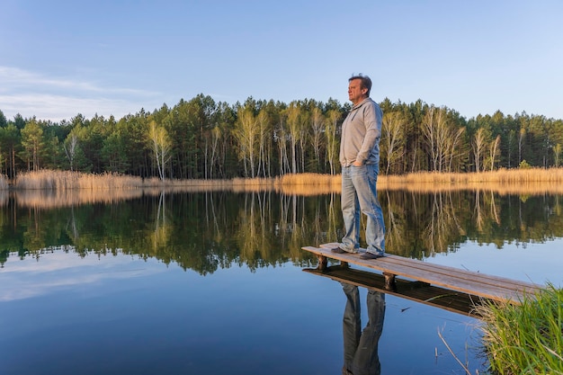 Man stands on a wooden pier near spring forest on a calm lake in Ukraine Nature and travel concept