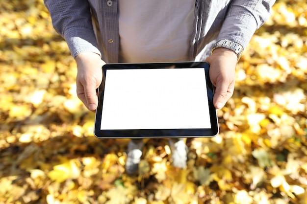 Man stands yellow leaves with tablet in his hands