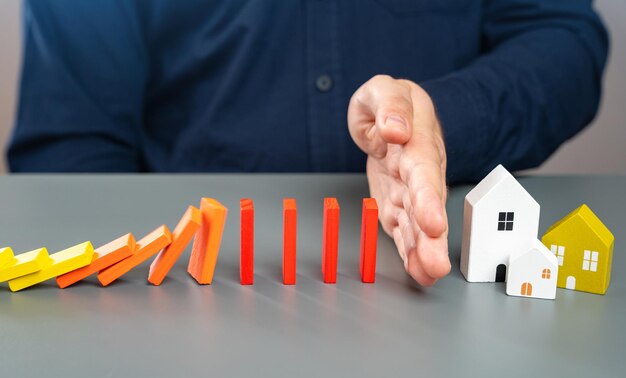 Photo a man stops dominoes falling on a house with his hand