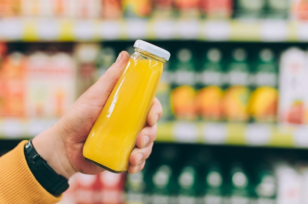 Man in a store holds a can of orange juice in his hand against the backdrop of a rack.