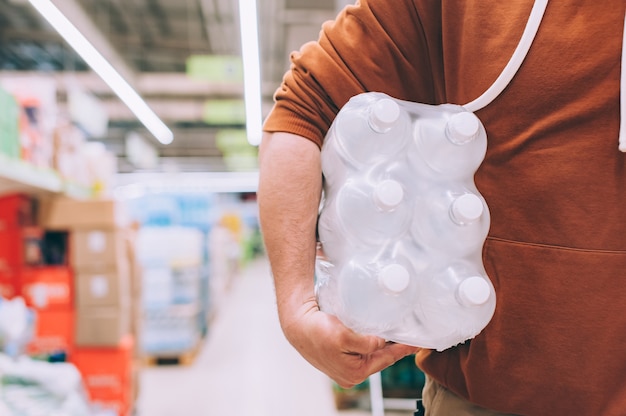 A man in a store holds a package of clean and transparent bottled water.