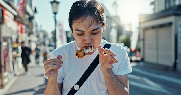 Photo man street food and eating kebab on walk on travel city and hungry for goheimochi with nutrition diet or lunch person rice snack and skewer on metro sidewalk vacation and urban road in japan