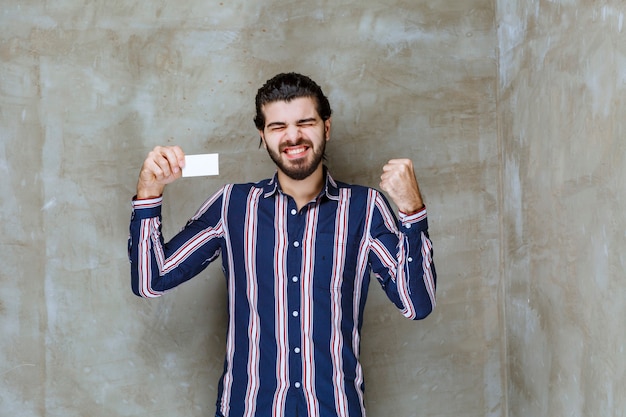 Man in striped shirt holding his business card and enjoying his new position