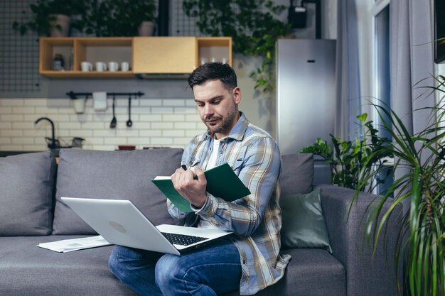 A man studying at home online uses a laptop sitting on the couch smiling