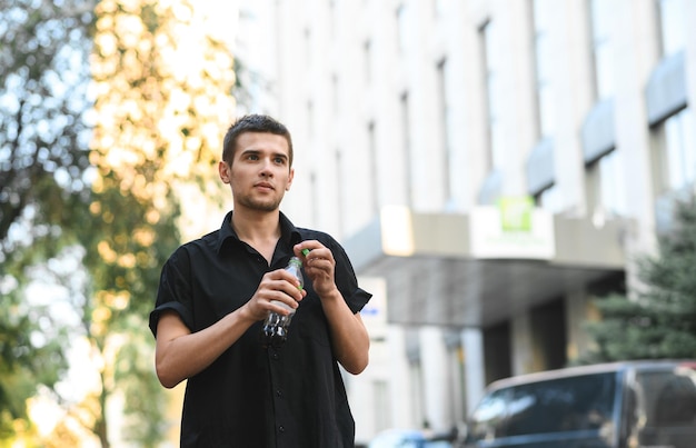 man in stylish casual clothes walking around the city with a bottle of sweet water in his hand