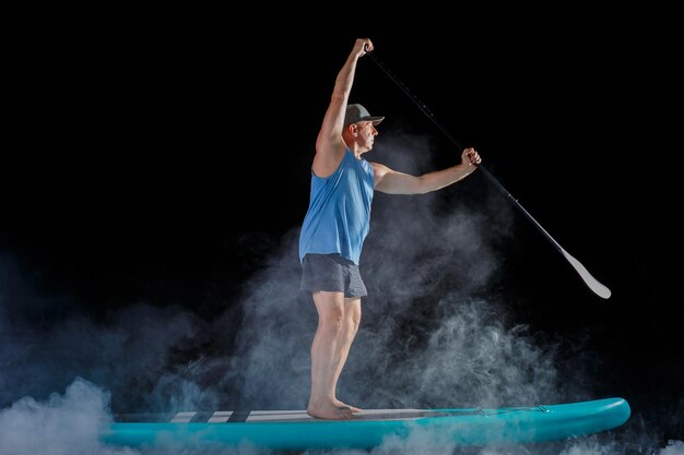 A man on a sub board with a paddle on a black background in the fog