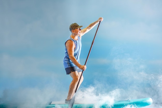 A man on a subboard with an oar paddles in thick fog against the background of clouds