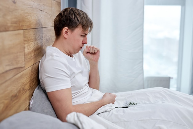 Man suffering from covid-19 symptoms lying on bed at home, high fever and coughing prevent him from living a normal life, he has to be on self-isolation. stay home