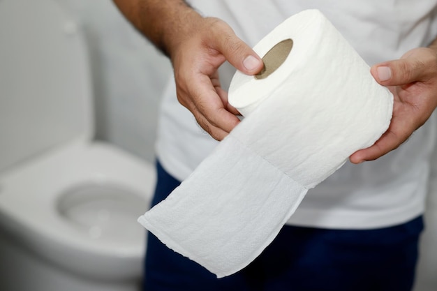 Man suffers from diarrhea hand hold tissue paper roll in front of toilet bowl constipation in bathroom Treatment stomach pain and Hygiene health care