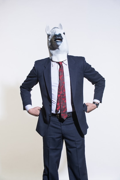 Photo a man in a suit and a horse mask on a light background. conceptual business background