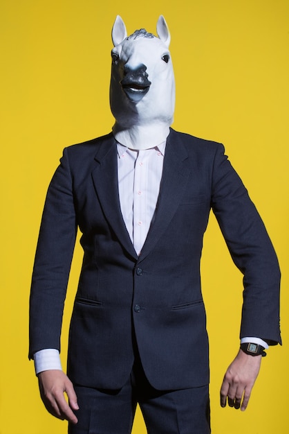 A man in a suit and a horse mask on a yellow background Conceptual business background