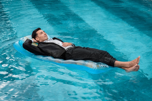 A man in a suit is resting in the pool on an inflatable blue mattress