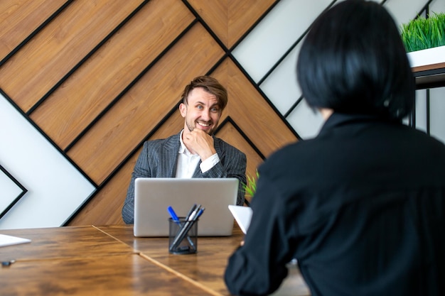 A man in a suit is sitting at his workplace and laughing with colleagues