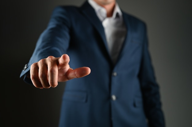 Man in suit pointing his finger at you and the camera, isolated on dark