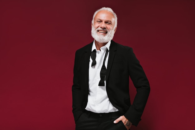 Man in suit and shirt smiling on burgundy wall