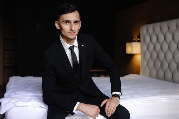 Photo a man in a suit sits on a bed in a dark room