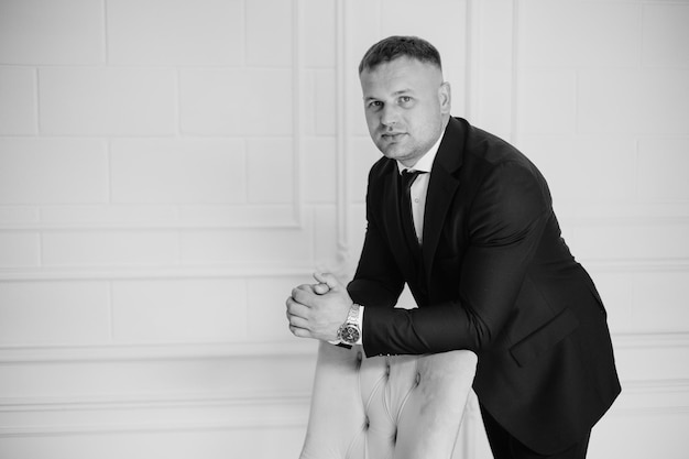 a man in a suit sits on a bench in front of a wall