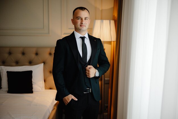 Photo a man in a suit stands in front of a bed with a lamp on it