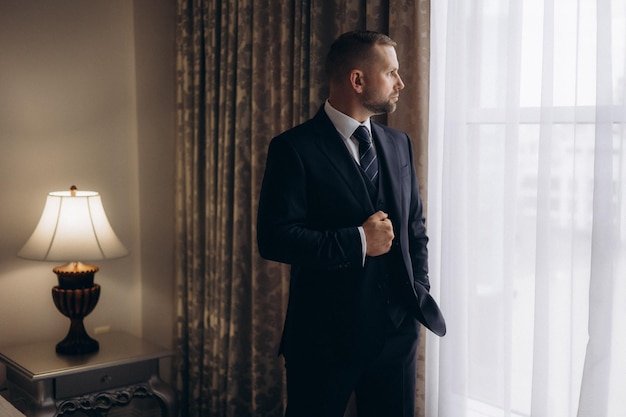 Photo a man in a suit stands in front of a window with a lamp and a lamp