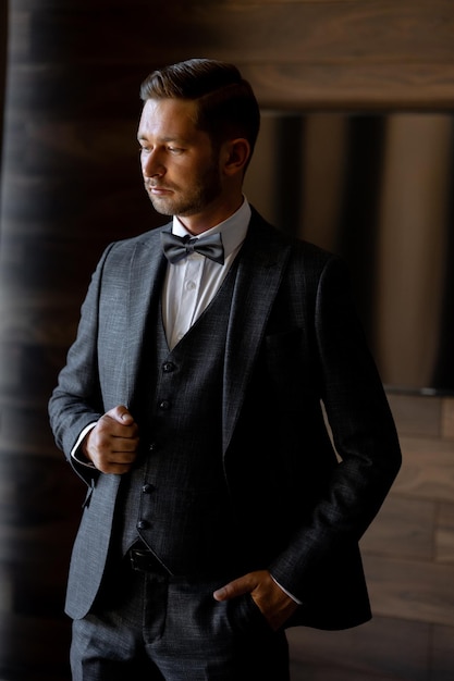 A man in a suit stands in front of a window.