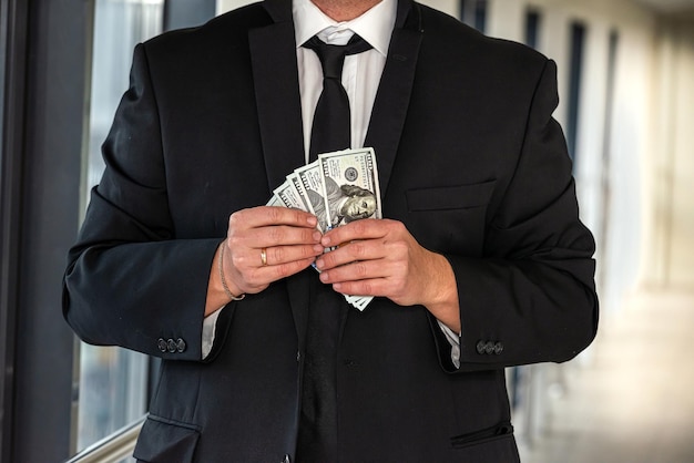 Man in suit stands in the hallway of the office with a large sum of dollars in his hands