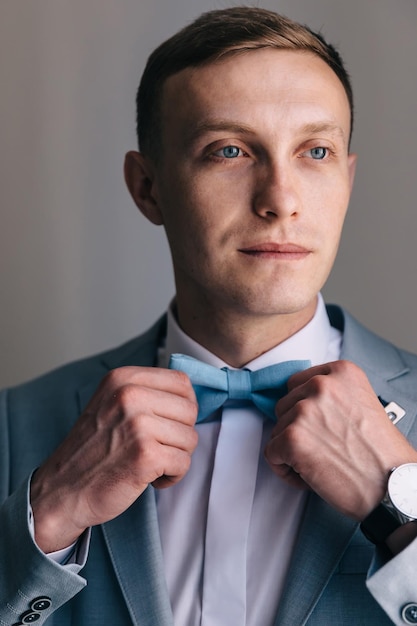 A man in a suit straightens his bow tie Morning preparation of the groom at home for the wedding