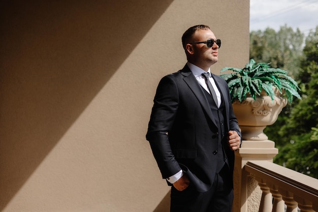 a man in a suit and sunglasses stands in front of a window