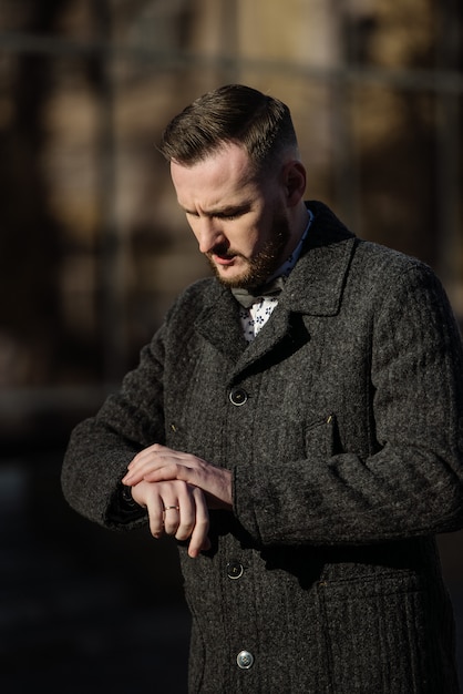 A man in a suit and sweater poses on the street.