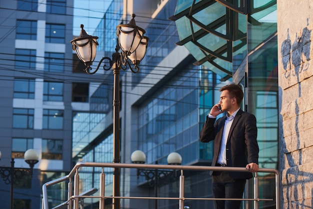 Man in suit talking on mobile phone against the building with a glass facade