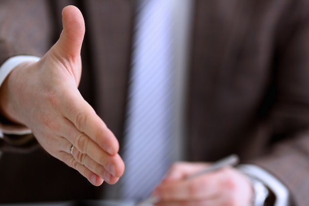 Man in suit and tie give hand as hello in office closeup. Friend welcome mediation offer positive introduction thanks gesture summit participate approval motivation male arm strike bargain