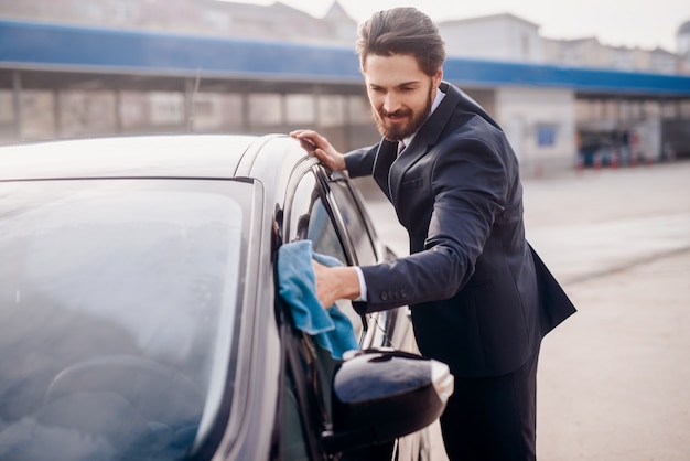 Man in suit wiping window on his car.