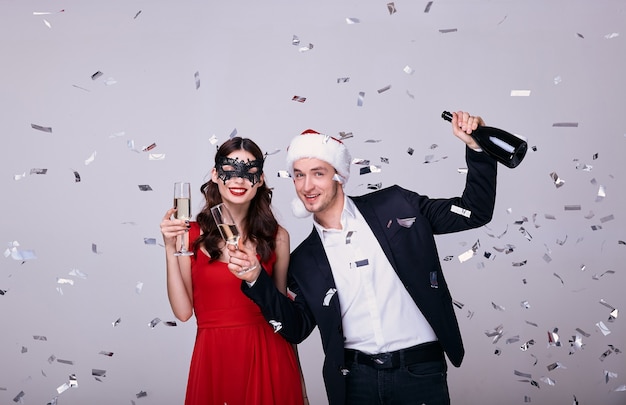 Man in suit and woman in red dress with champagne glasses isolated on gray background with confetti