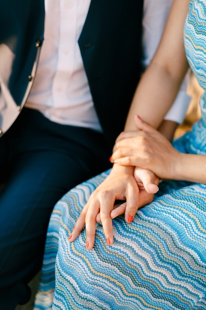 Man in a suit and woman in a striped blue dress are sitting holding hands